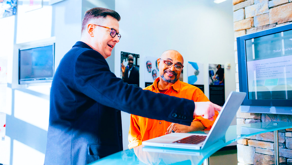 Two smiling male business colleagues looking and pointing at laptop on standing desk