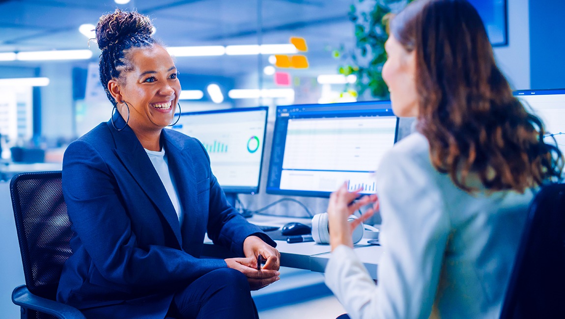 Two female colleagues chatting ta a desk