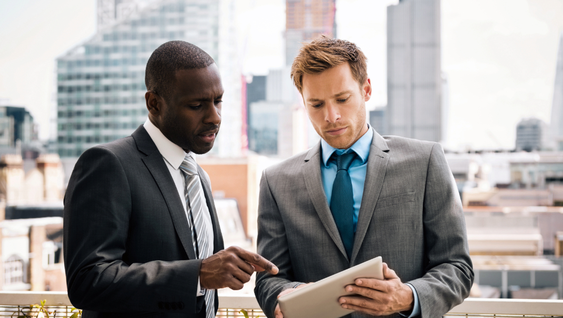 Two male colleagues studying a report with buildings in the background