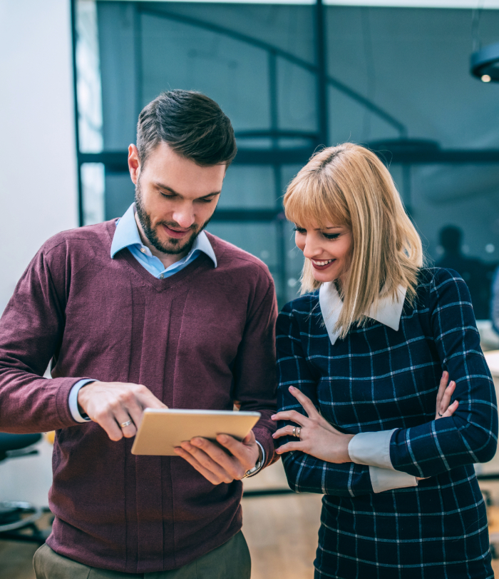 Male and female colleague smiling while looking at digital tablet in modern office